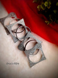 Display of 7 oxidized German silver bangles featuring geometric flared edges and leaf textures resting on white plush fur and red cloth background.Distinctive flared outer frames with delicate scroll filigree that add volume and drama to the wrist.Embossed motif bands that capture light and accentuate the oxidized antique finish.  