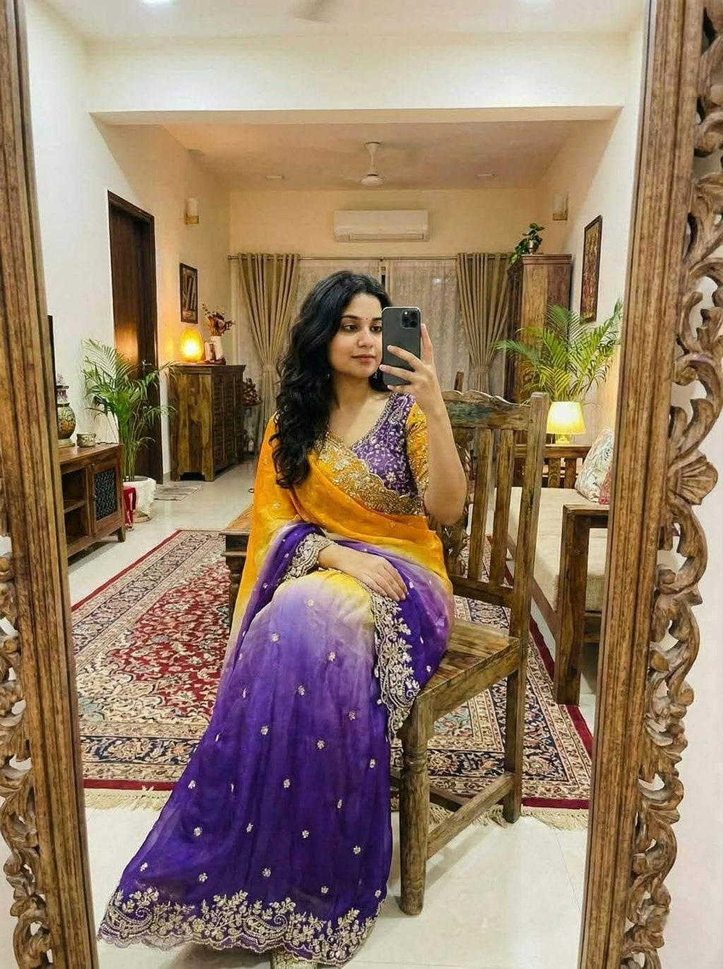 Mirror selfie of a woman wearing a dual-tone mustard yellow and deep purple satin saree with gold embroidered scalloped borders and a matching purple embroidered blouse.Dynamic yellow-to-purple ombre transition that provides instant visual pop.  Delicate metallic sequin work framing the saree edges with elegant sheen.