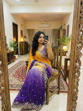 Mirror selfie of a woman wearing a dual-tone mustard yellow and deep purple satin saree with gold embroidered scalloped borders and a matching purple embroidered blouse.Dynamic yellow-to-purple ombre transition that provides instant visual pop.  Delicate metallic sequin work framing the saree edges with elegant sheen.