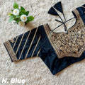 A navy blue blouse with intricate gold embroidery and striped detailing on the sleeve, laid flat on a beige textured carpet next to small white flowers.