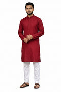 Man wearing a maroon red kurta with white pants standing in front of a white background