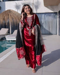 Woman wearing a luxurious maroon ice velvet long top and matching pants, styled with a contrasting dark decorative dupatta featuring ornate embroidery and a resort/poolside background.  