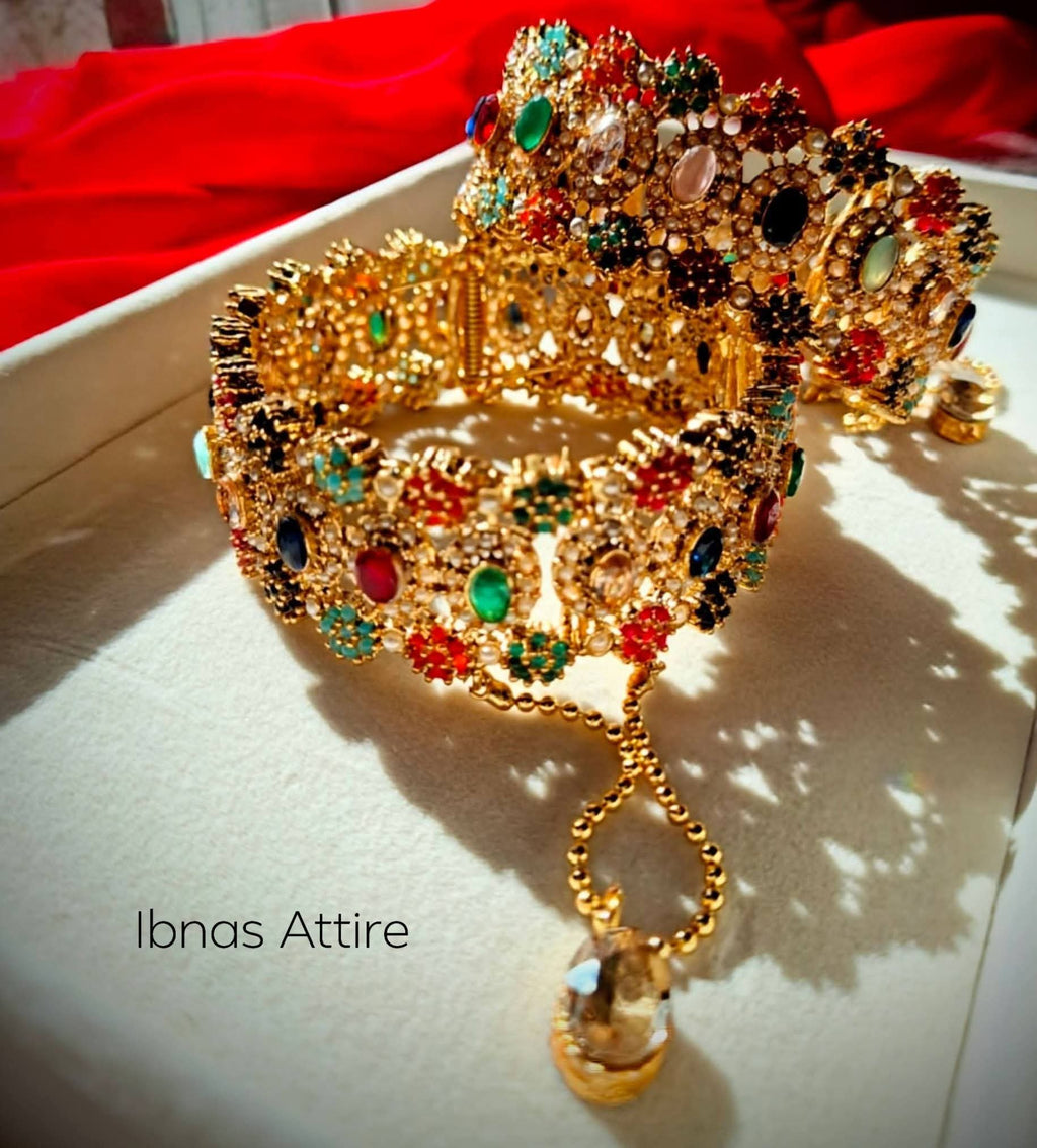 Pair of wide antique gold bangles studded with multi-colored semi-precious stones and micro pearls, featuring hanging dangles/chains, resting inside a white box against a red backdrop.Built-in screw mechanism with attached safety dangles, allowing easy slip-on without squeezing your hand.