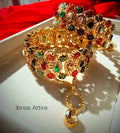 Pair of wide antique gold bangles studded with multi-colored semi-precious stones and micro pearls, featuring hanging dangles/chains, resting inside a white box against a red backdrop.Built-in screw mechanism with attached safety dangles, allowing easy slip-on without squeezing your hand.