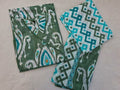 A folded 3-piece Jaipuri cotton set with a green, white, and turquoise ikat pattern, laid flat on a light beige textured background.