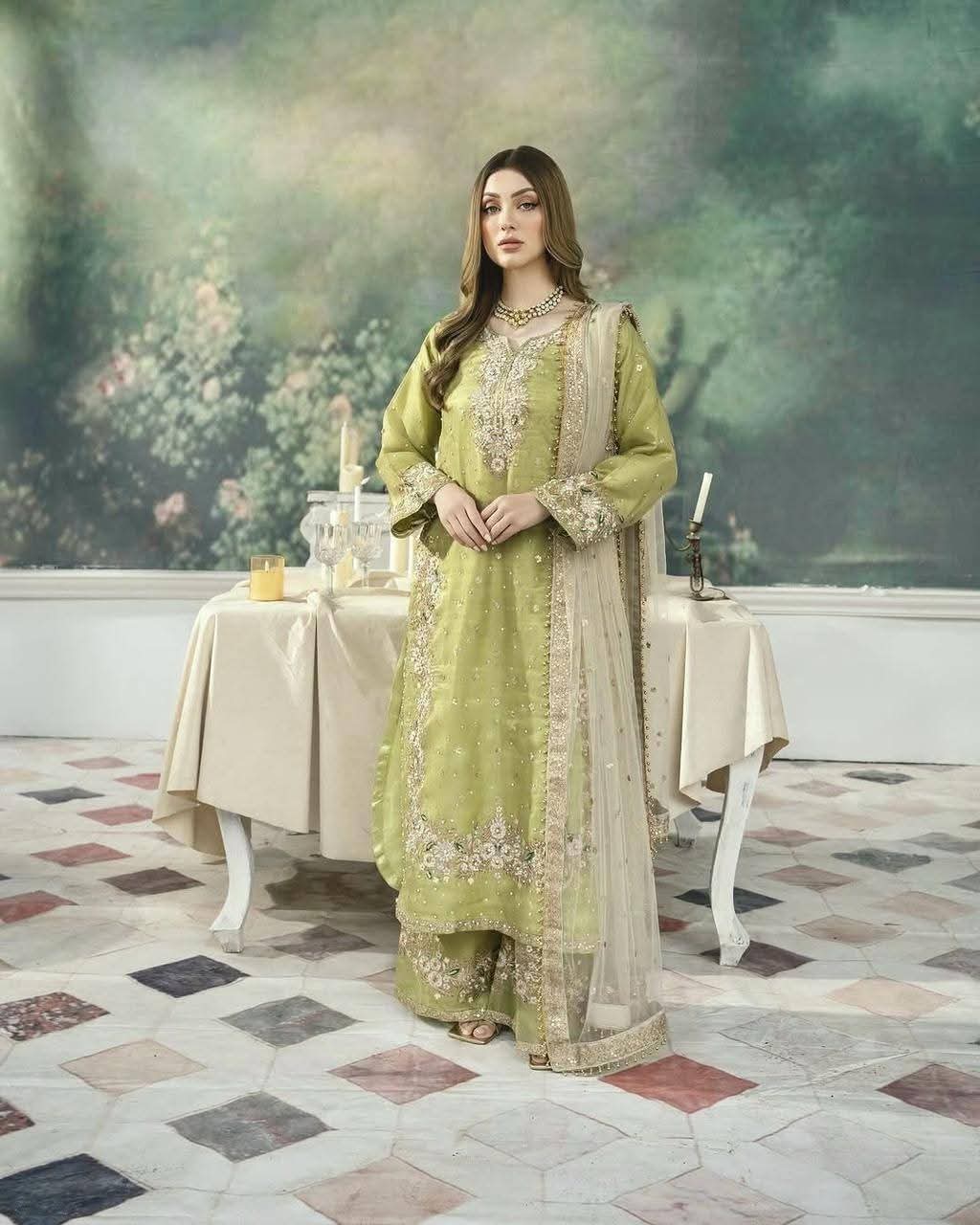Woman in a green traditional outfit standing in a decorated room with a table and floral decorations.