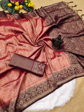 Flat lay of a soft silk saree with dusty rose gold body woven in floral jacquard patterns, dark wine maroon contrast pallu with tassels, and folded contrast blouse fabric.Complementary wine maroon blouse block woven with geometric grid motifs and matching border strip.