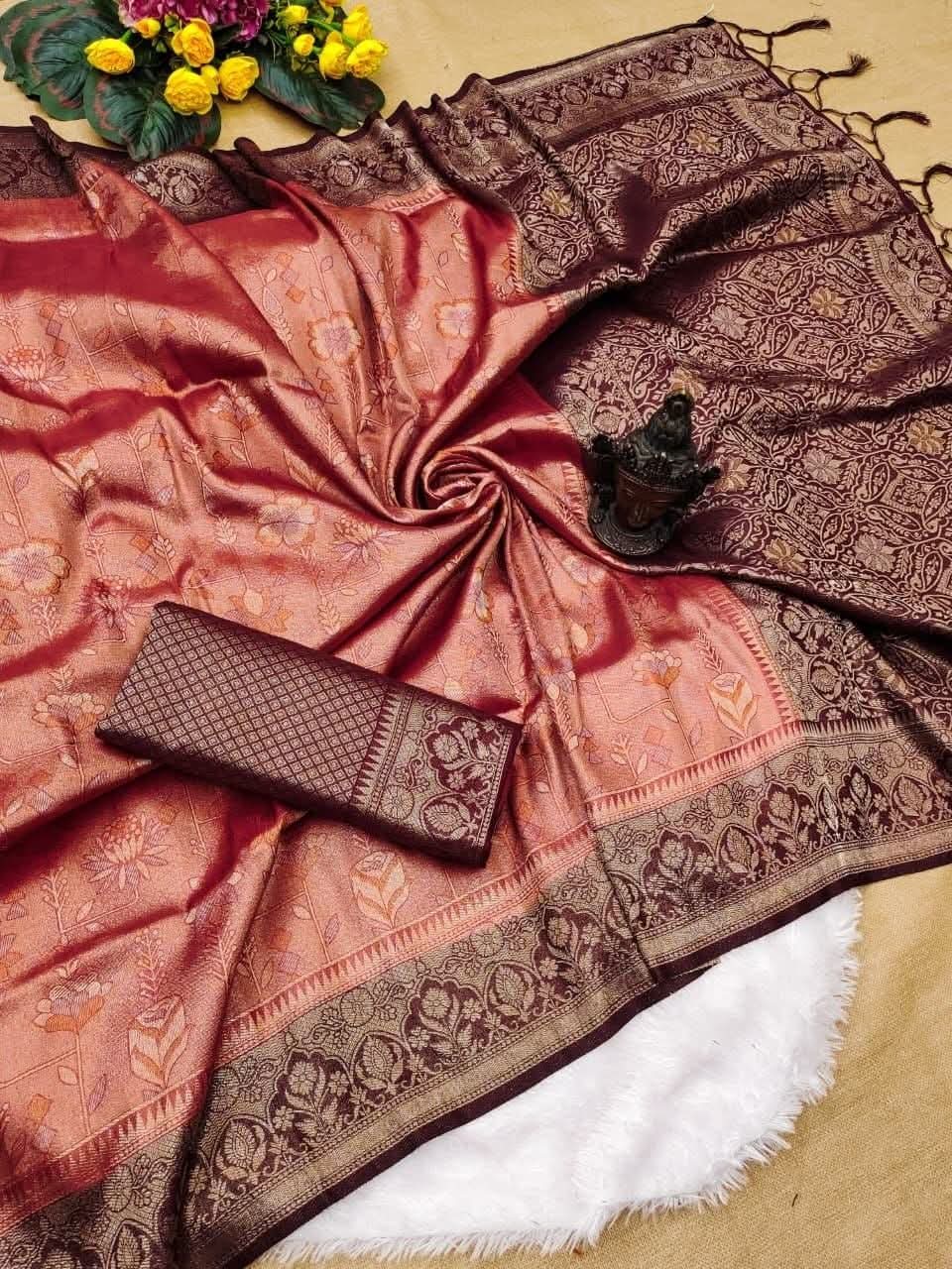 Flat lay of a soft silk saree with dusty rose gold body woven in floral jacquard patterns, dark wine maroon contrast pallu with tassels, and folded contrast blouse fabric.Complementary wine maroon blouse block woven with geometric grid motifs and matching border strip.