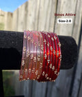 Stack of translucent glass bangles split between soft baby pink and deep crimson red with gold sequin accents displayed on a black velvet bar outdoors against a wooden fence.