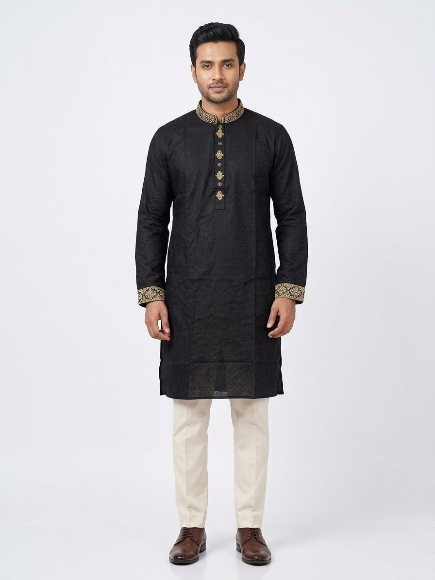 Full-length front shot of a man wearing a black cotton panjabi with gold embroidered collar and cuffs, paired with off-white trousers and brown dress shoes.Matching embroidery motifs across the mandarin band collar, front placket, and wrist cuffs. 