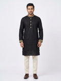 Full-length front shot of a man wearing a black cotton panjabi with gold embroidered collar and cuffs, paired with off-white trousers and brown dress shoes.Matching embroidery motifs across the mandarin band collar, front placket, and wrist cuffs. 