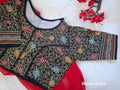 Black malai cotton blouse laid flat over a vibrant red drape on a soft white fur surface, displaying detailed multicolored Kantha embroidery and a front hook closure. Elegant geometric and paisley Kantha borders highlighting the sleeve cuffs and lower hem. 