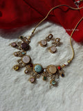 Antique gold-plated necklace set with oval and round multi-colored cabochon semi-precious stones and matching earrings displayed on a white faux-fur backdrop beside a red drape.Bezel-set round cabochon stones in complementary earth and pastel tones balanced across textured antique gold frames.Subtle pearl droplets and delicate cubic zirconia/crystal halo trims surrounding each central stone.  Soft woven gold cord allowing you to wear it as a close-fit choker or a longer princess-length necklace.