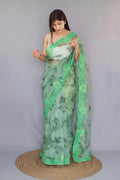 A woman models a light green organza silk saree. The saree features green floral patterns and a contrasting bright green embroidery work border