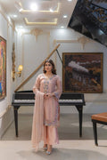 Model wearing a dusty blush pink long-sleeved embellished chiffon shirt with matching wide trousers and dupatta indoors beside a grand piano.Intricate hand-embellished beadwork, pearls, and delicate embroidery along the V-neckline, sleeves, and side borders.Light, graceful drape with broad trousers creating an elongated, elegant silhouette.Rich, textured Banarsi Katan base adds depth and a subtle luster under the translucent chiffon top. 