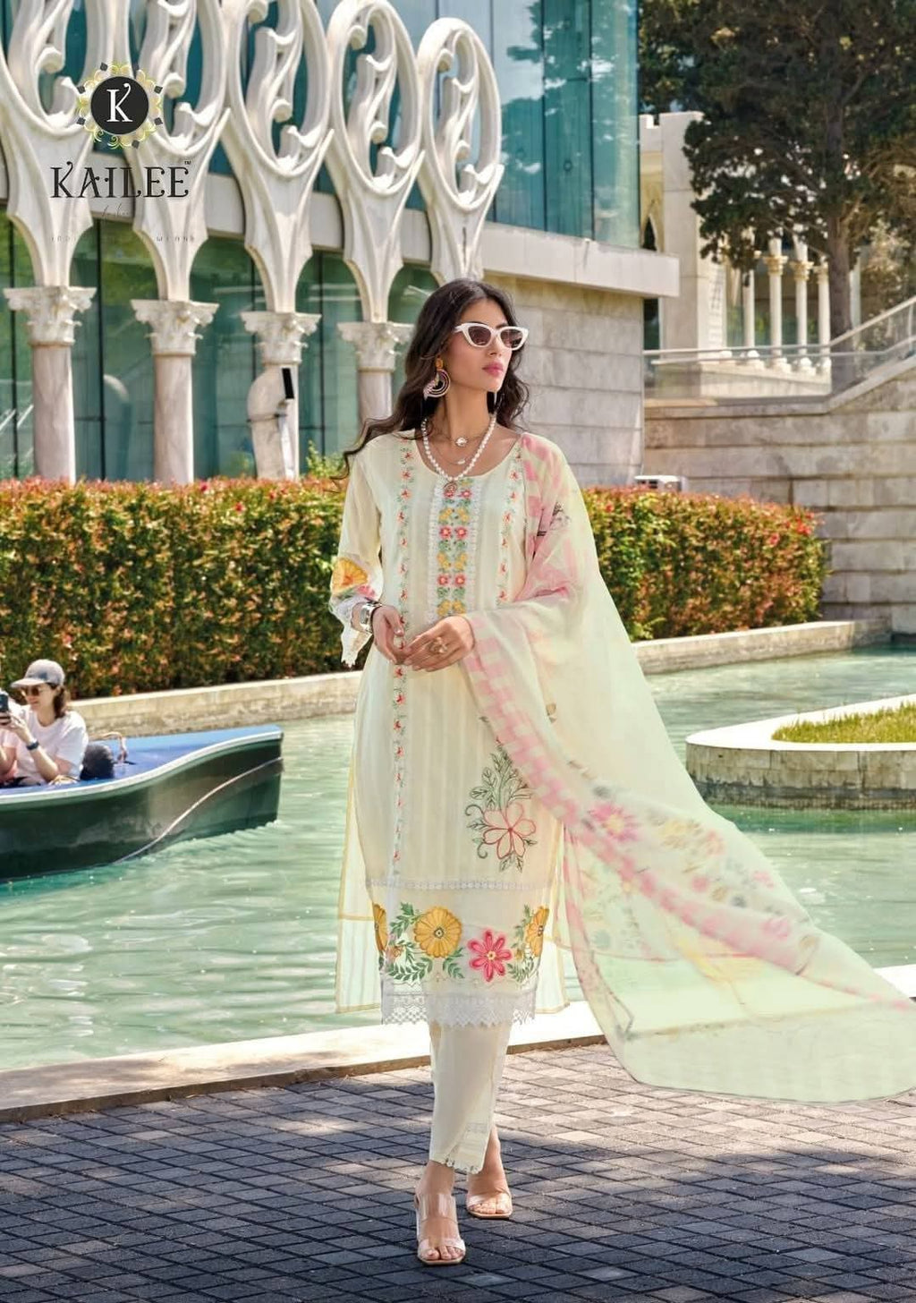 Woman in a floral dress standing in front of a decorative fountain with 'KAILIE' branding.