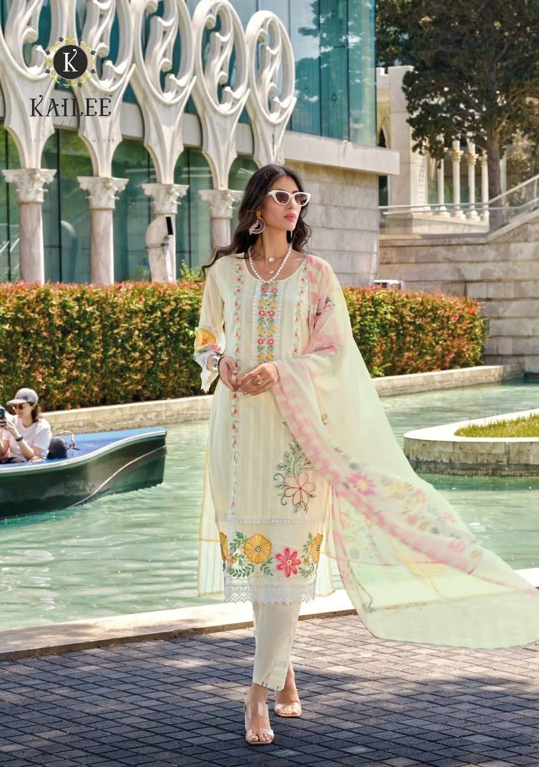 Woman in a floral dress standing in front of a decorative fountain with 'KAILIE' branding.