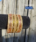Stack of translucent peach pink and golden amber glass bangles with glittery gold borders and sequin accents displayed on a black velvet bar outdoors against a wooden fence.Soft harmonizing shades of peach pink and golden amber that complement neutral and pastel outfits effortlessly.