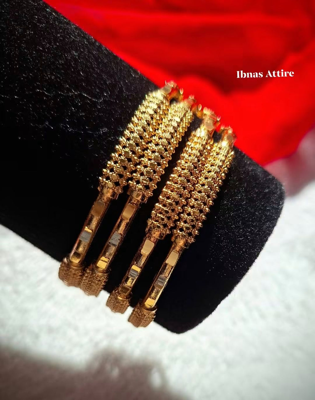 Set of four gold-plated textured bangles displayed on a dark velvet stand against a red background.