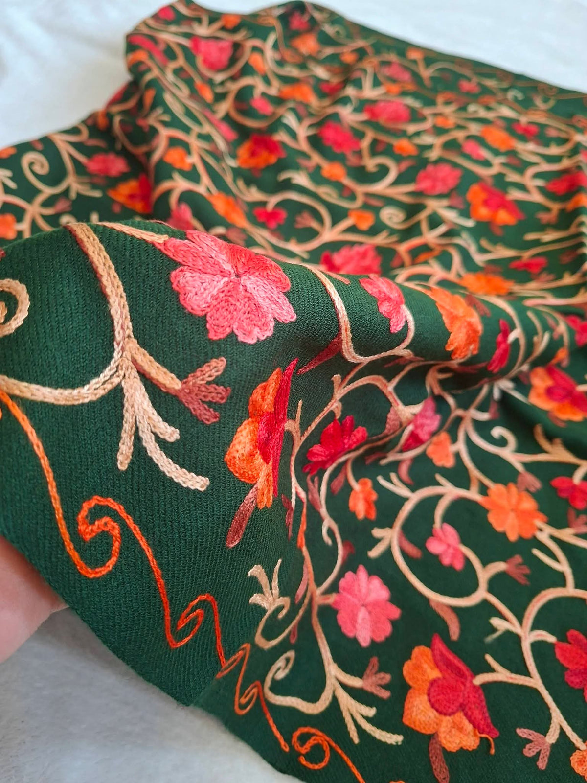 A deep green multicolour embroidery worked woolen shawl held by a hand