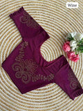 A wine-colored lycra blouse top with gold zari embroidery and ruffled sleeves, laid flat on a circular woven straw mat with pink roses as a decorative prop.