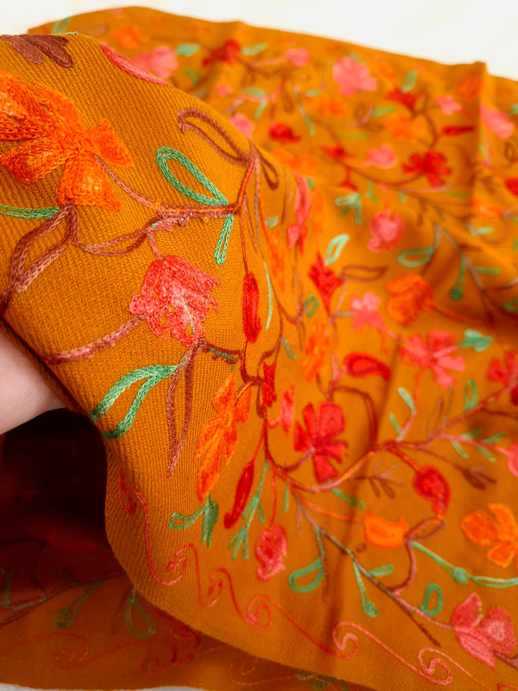 A mustard color wooled shawl with Multicolor Embroidery work held by a hand