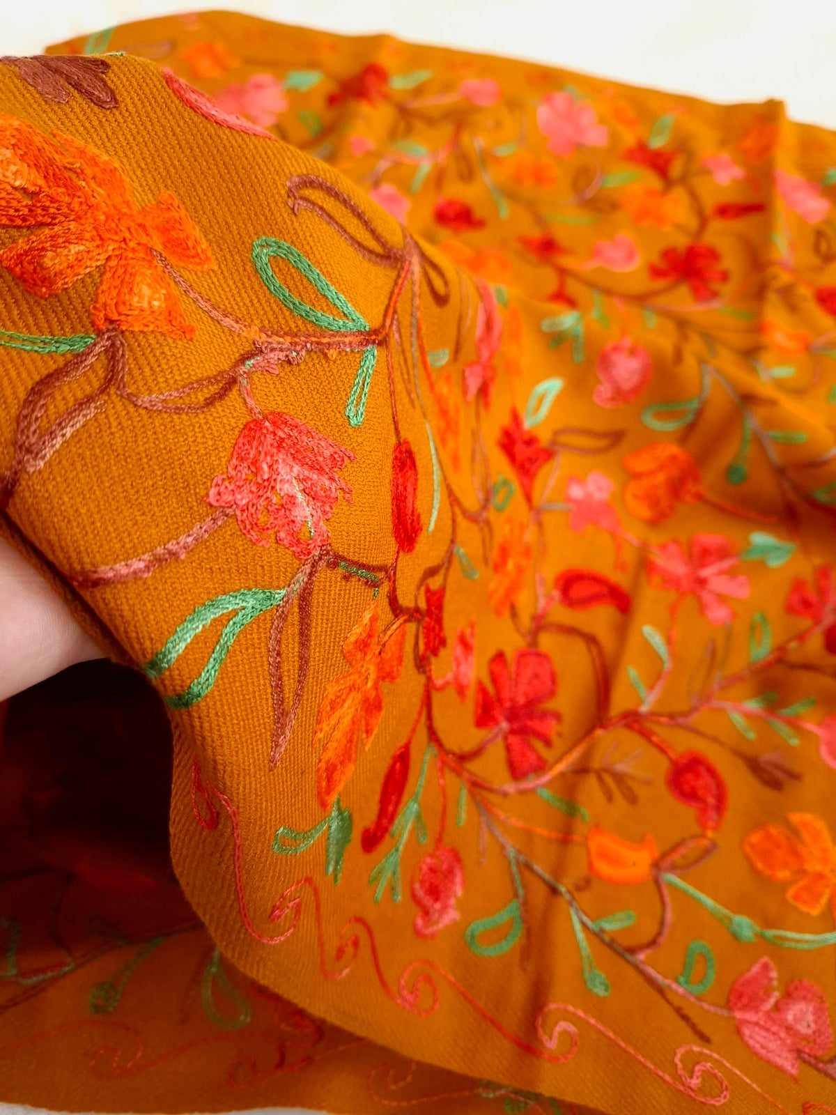 A mustard color wooled shawl with Multicolor Embroidery work held by a hand