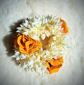 Artificial white mogra flower hair bun gajra decorated with yellow fabric roses on a white surface 