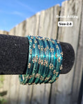 Stack of translucent aqua teal / ocean blue-green glass bangles with gold sequin accents displayed on a black velvet bar outdoors against a wooden fence.  Smooth glass construction that produces a traditional, melodious chime when worn.  