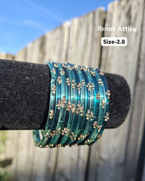 Stack of translucent aqua teal / ocean blue-green glass bangles with gold sequin accents displayed on a black velvet bar outdoors against a wooden fence.  Smooth glass construction that produces a traditional, melodious chime when worn.  