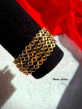 Set of four gold-plated Continuous flowing geometric wave-textured bangles displayed on a black velvet stand against a red backdrop.