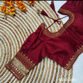 A maroon blouse top with gold embroidered borders and tassel ties, laid flat on a woven circular rug with orange flowers in the corner. The word MAROON appears in the bottom right.