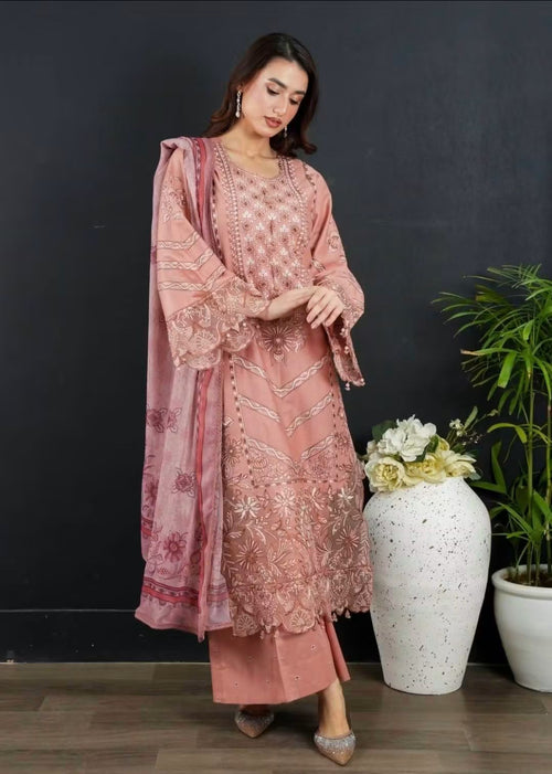 A woman models a dusty pink Traditional Pakistani Embroidered 3-Piece Suit.Seamlessly matched trousers and a printed complementary dupatta to complete the designer look.Dense multi-tonal threadwork creating rich geometric and floral patterns across the front.Wide bell sleeves finished with elaborate cutwork embroidery and delicate dangling beads.