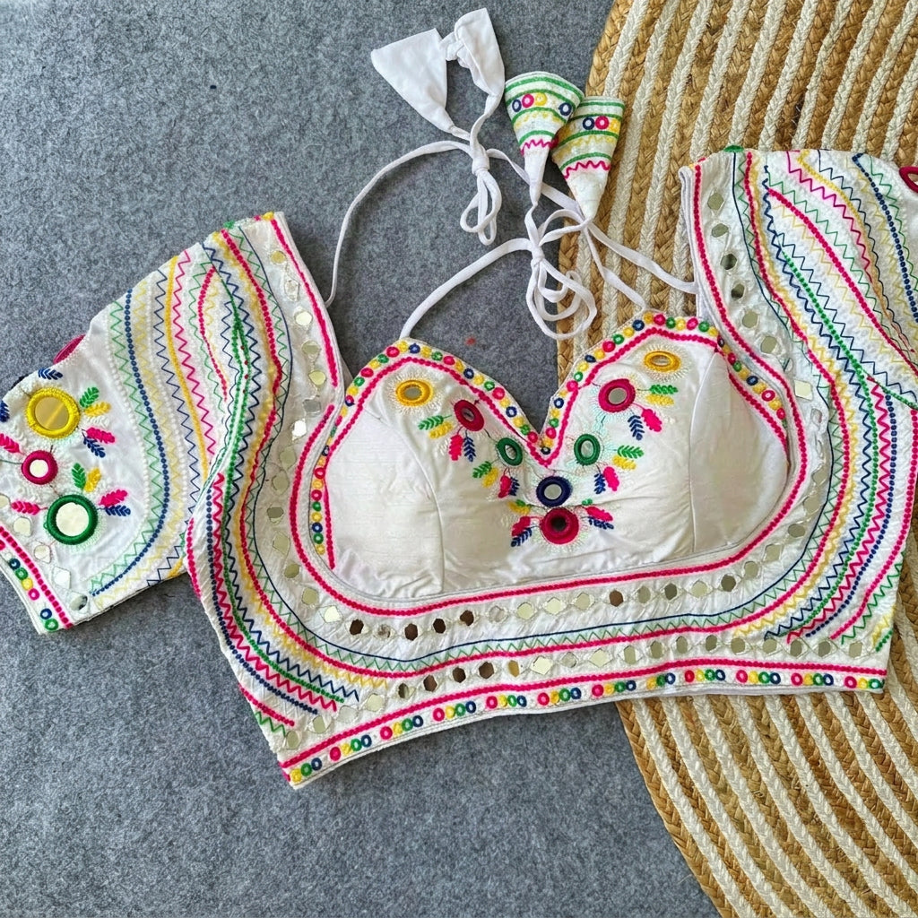 White silk readymade blouse with colorful Gamthi thread embroidery, real mirror work, Mumtaz sweetheart neckline, 12-inch sleeves, and latkan ties displayed on a jute rug.
