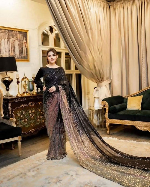 Woman in a black and gold dual tone Sequins georgette saree standing in an elegant room with decorative furniture.