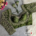Olive green pure Vichitra silk readymade blouse with heavy gold zari embroidery, full long sleeves, sweetheart Mumtaz neck, back open style, and fan latkans displayed on a grey felt background.