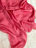 A draped coral pink satin silk hijab, laid out on a white faux fur surface.