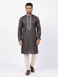 Full-length shot of a man wearing a dark puce Jacquard silk kurta with self-woven patterns and silver-grey embroidered neck placket, paired with cream trousers and brown dress shoes.