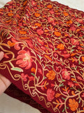 A wool blend all over embroidery worked kashmiri shawl in maroon color held by a hand