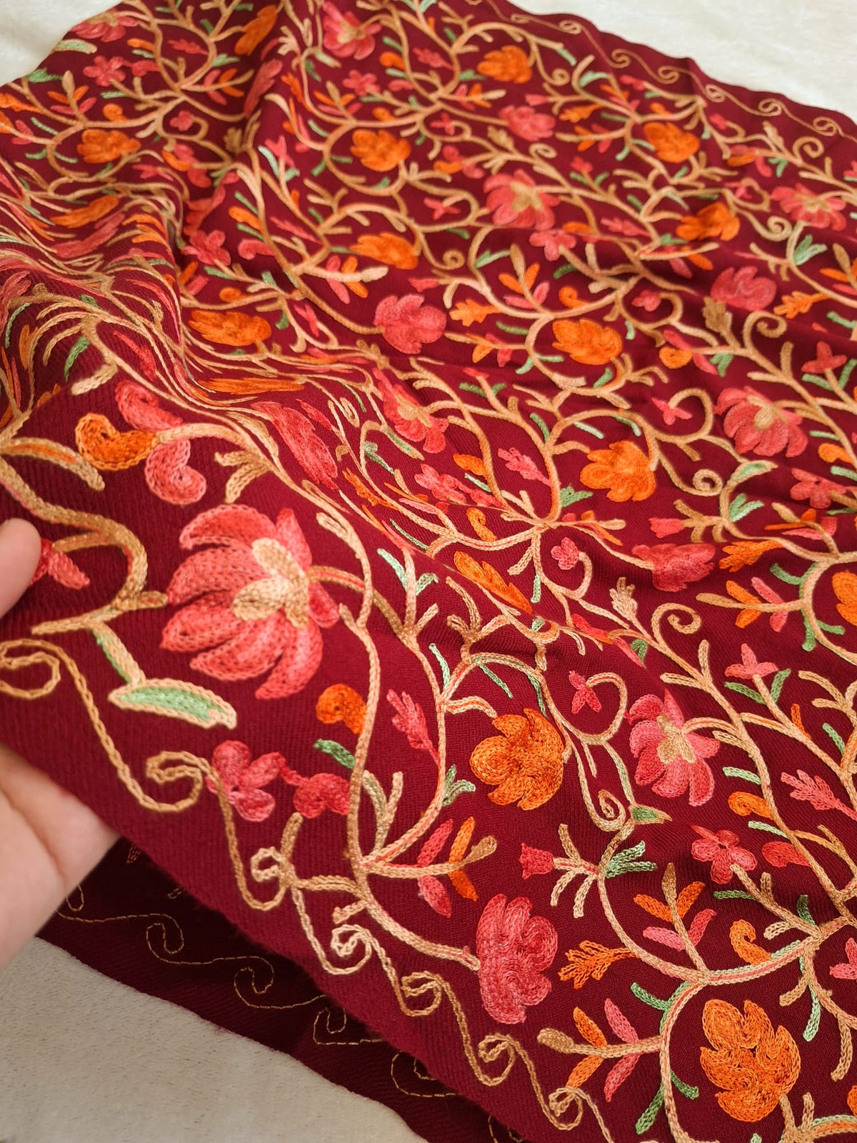 A wool blend all over embroidery worked kashmiri shawl in maroon color held by a hand