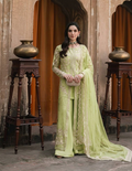 A woman stands in a traditional courtyard wearing a light lime green pakistani salwar kameez suit 