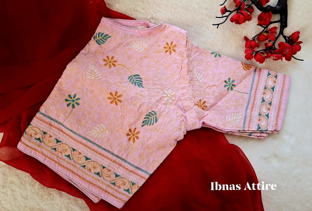 Soft baby pink malai cotton blouse laid flat over a deep red drape on a soft white fur background, highlighting fine Kantha stitch embroidery and a front hook closure.Gentle, breathable fabric tailored for all-day comfort during events.Delicately layered running stitches forming swirling vines, leaves, and floral centers on a soft pastel backdrop. 