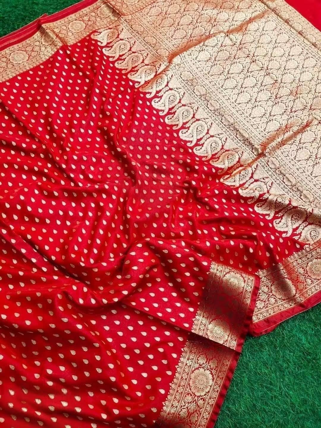 Traditional Banarasi Katan Silk Red saree-Intricate metallic gold jacquard weaving featuring traditional motifs across the body and heavy border framing.Vibrant red dual-tone satin-silk fabric, scattered gold zari bootis, rich gold woven pallu/border resting on green surface.