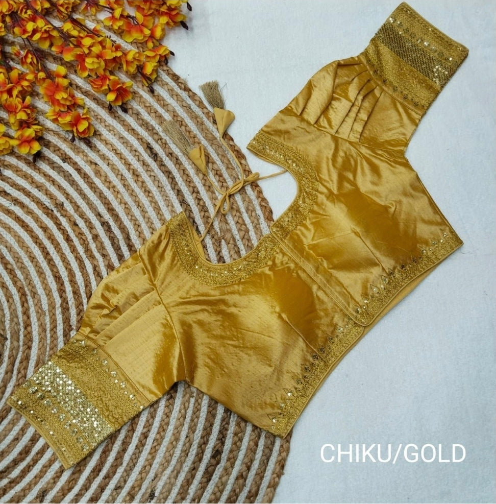 Metallic chiku/gold Jasmin silk saree blouse displayed flat on a circular jute mat, featuring gold sequence embroidery on the neck, hem, and puff sleeve cuffs. Fine gold sequence and matching threadwork defining the round neck and bottom hemline. 