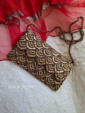 A rectangular clutch bag with an intricate gold and brown scalloped beaded pattern, resting on a white faux fur surface with red sheer fabric in the background. The brand name 'Ibnas Attire' is visible as a watermark in the bottom left corner.