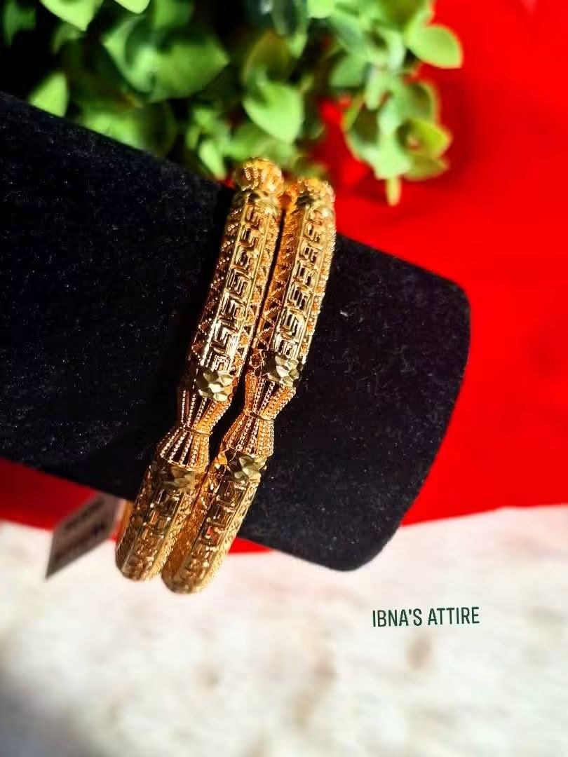 Gold plated bangles on a black stand with a red and green background