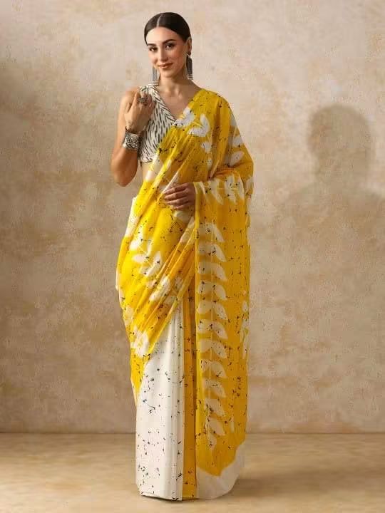 A woman models a yellow and white printed pure soft mul mul cotton saree with a patterned blouse, standing against a textured beige studio backdrop.