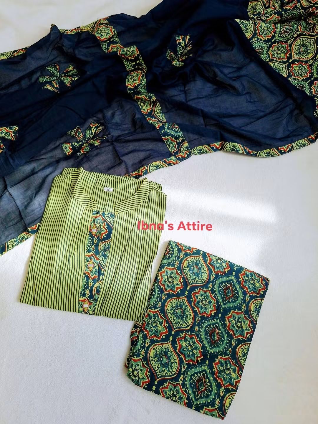 Featuring a Traditional Ajrak Printed patchwork 3-Piece Suit-in ive green, blue color -Lightweight, breathable fabric engineered for all-day ease and a smooth silhouette.Deep-toned printed dupatta featuring classic heritage geometric patterns and borders.Hand-finished fabric patch detailing adding rich texture to the green striped base.