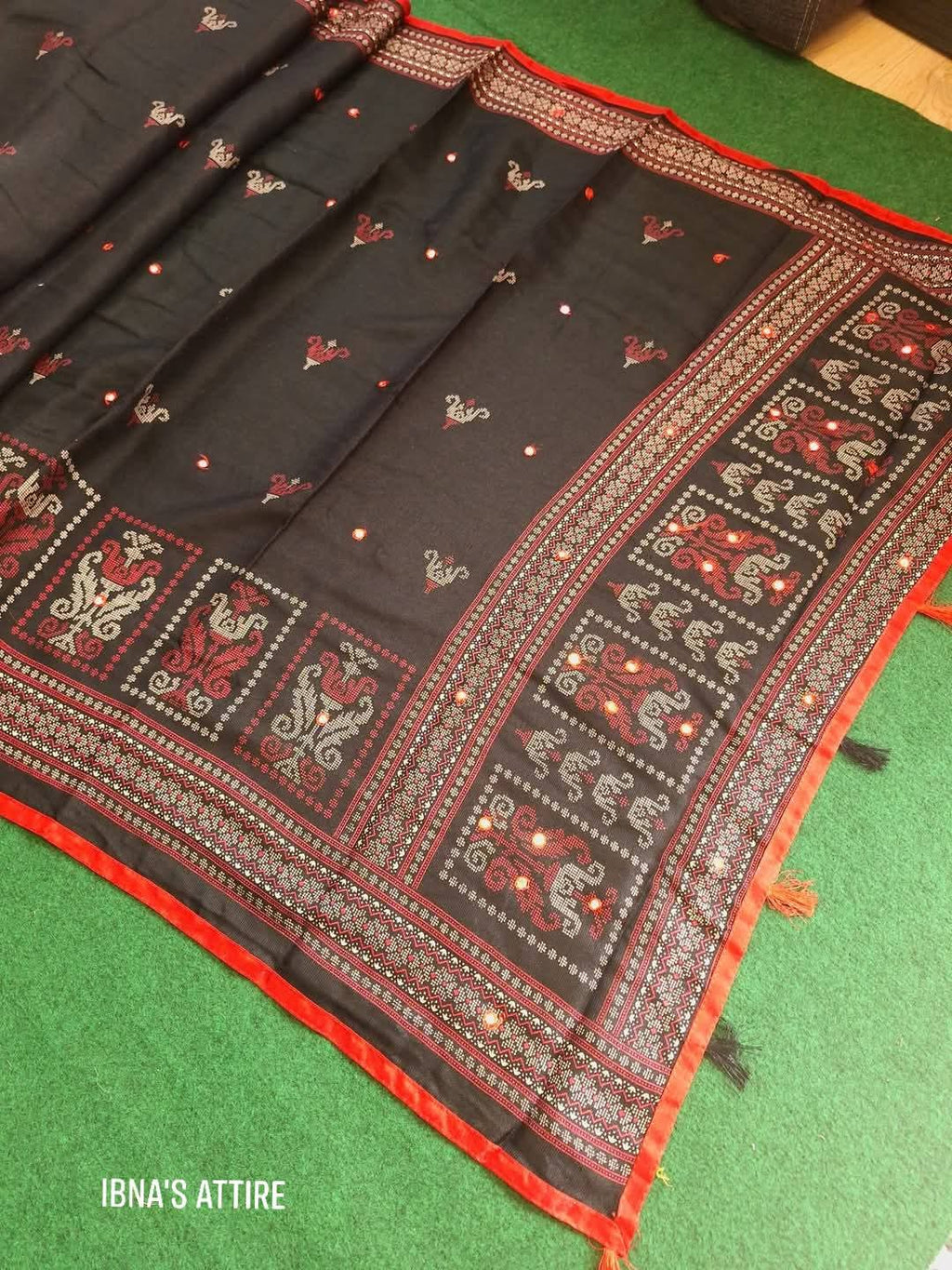 Black saree with red and gold patterns on a green surface