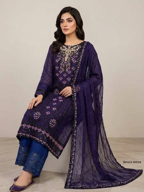 A woman models a traditional three-piece salwar kameez suit in deep purple. The set includes a heavily embroidered Pakistani chiffon purple kameez top, matching purple silk pants, and a sheer purple Chiffon dupatta with floral embroidery and metallic borders.